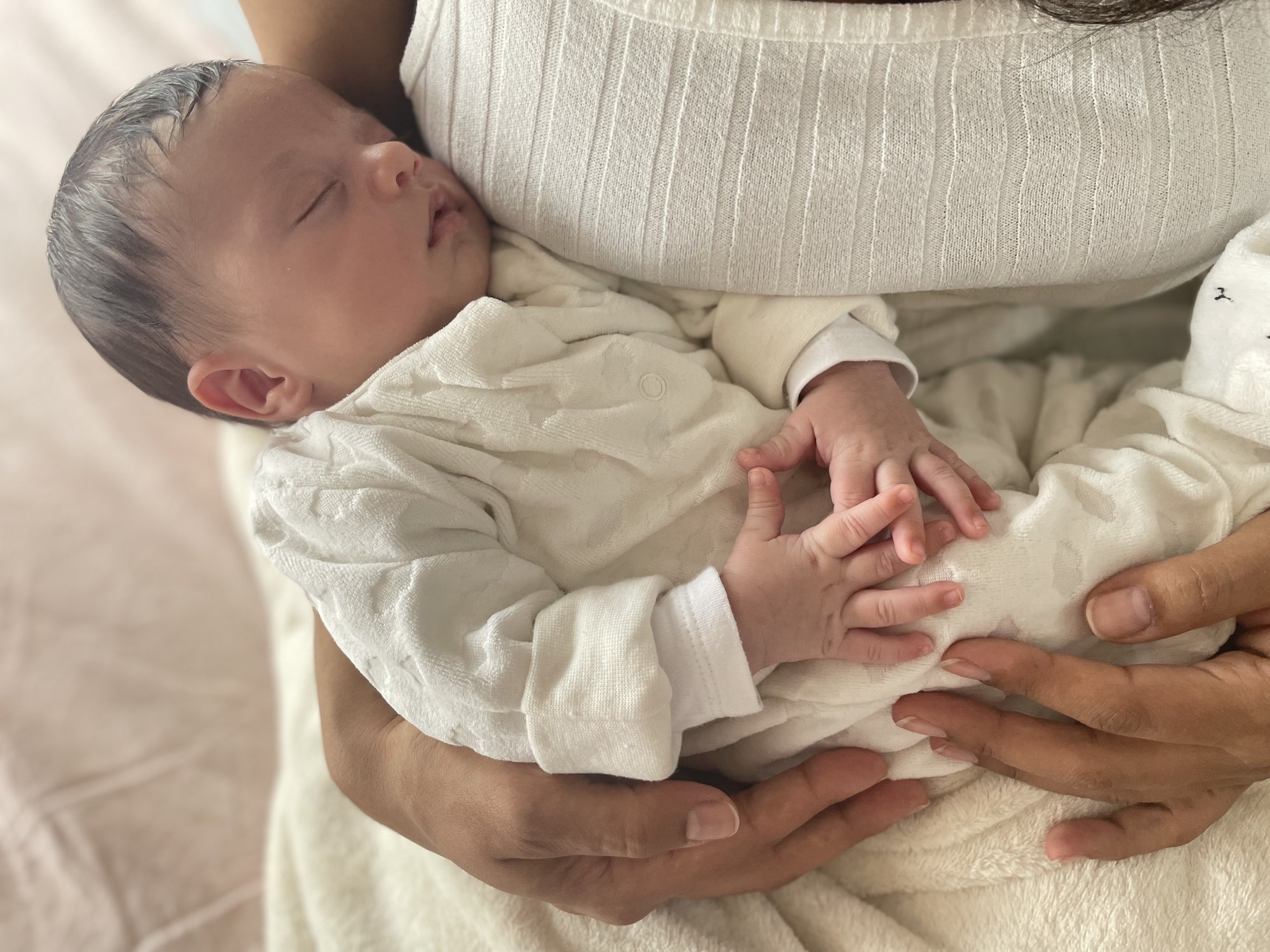 Neugeborenes schläft entspannt in den Armen der Mutter