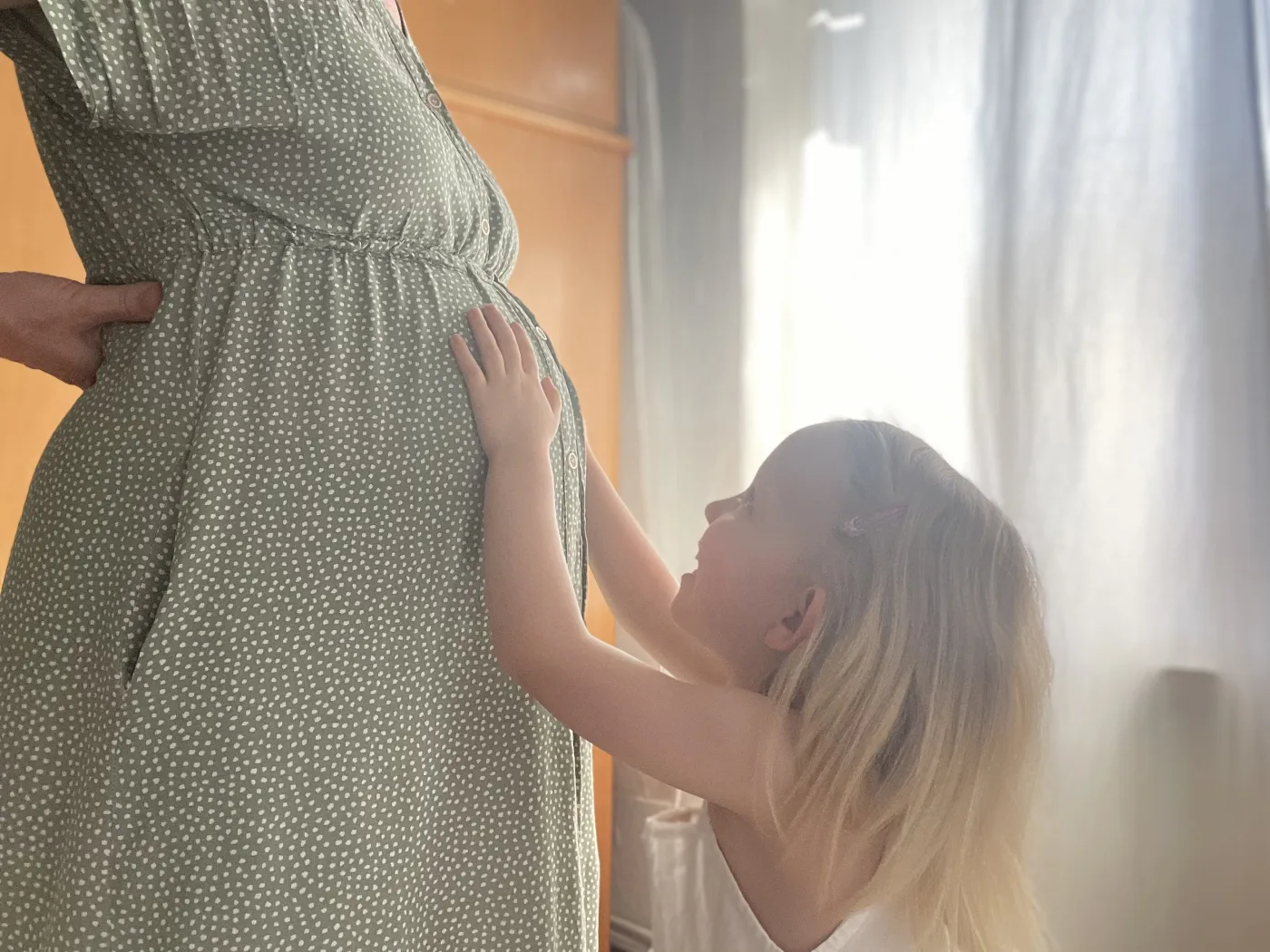 Schwangere Mutter, deren Geschwisterkind die Hand an den Babybauch legt