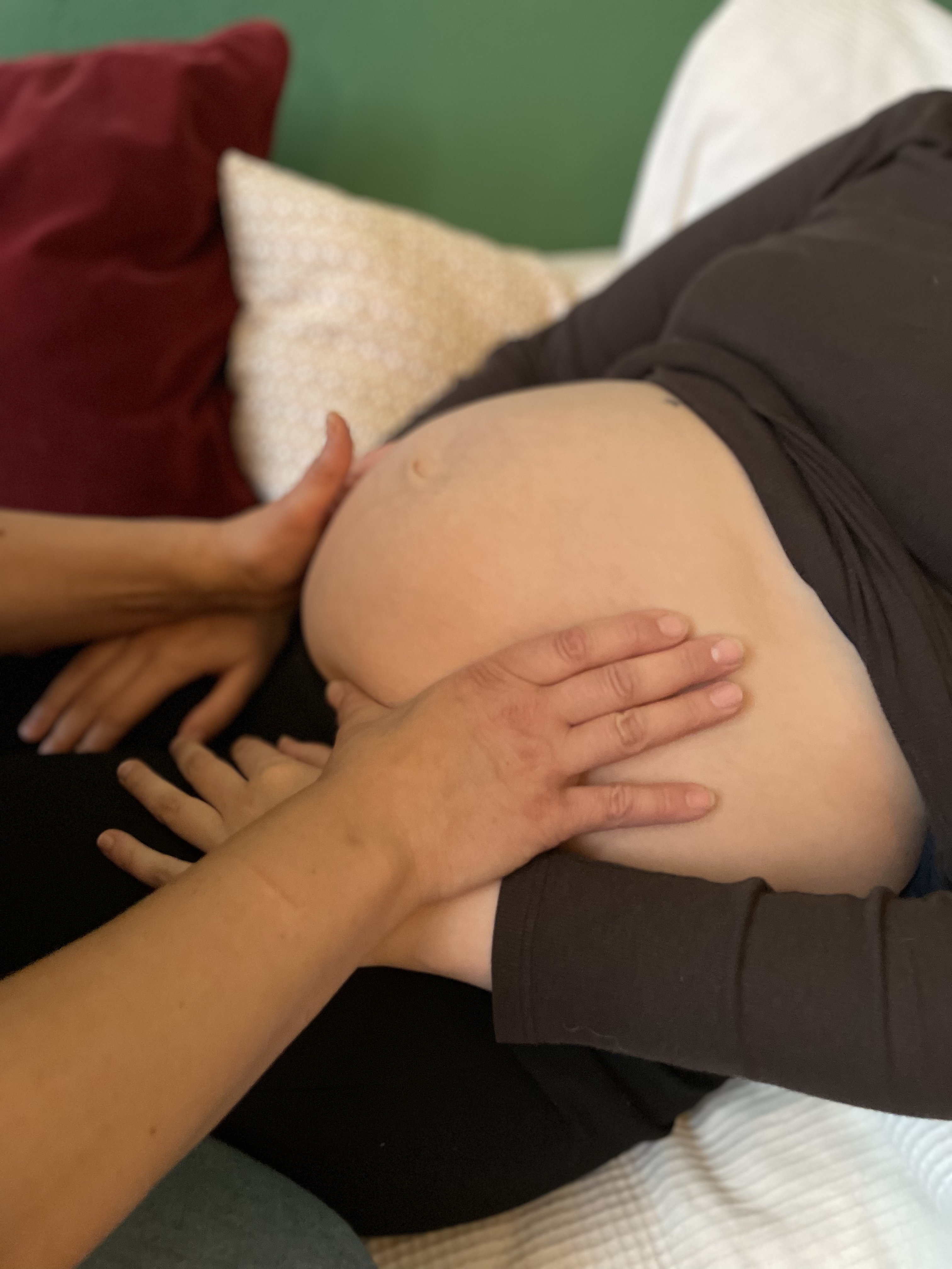 Hebamme tastet mit beiden Händen sanft den Babybauch einer Schwangeren